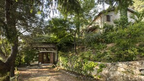 Un rústico edificio de piedra con techo de tejas tradicionales, rodeado de abundante vegetación y árboles.