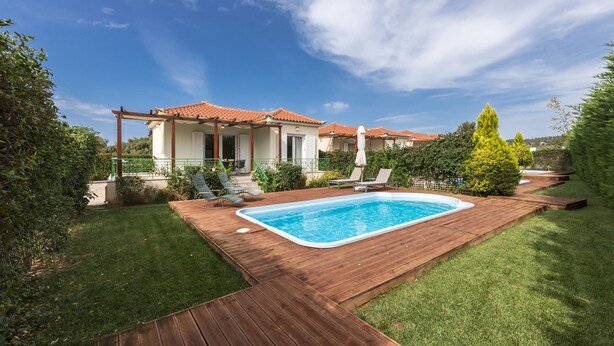 A pool with a wooden deck, surrounded by a well-maintained lawn and a house with a tiled roof. - Sun, Sand & Seclusion - Artemis with Private Pool (Pylos-Nestoras)