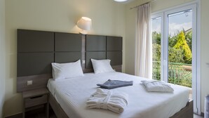 A neatly made bed with white linens and towels, a bedside table with a lamp, and a balcony with a view of greenery. - Sun, Sand & Seclusion - Artemis with Private Pool (Pylos-Nestoras)
