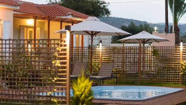 Zona de piscina con sillas de descanso y sombrillas, rodeada por una valla de madera.