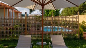 Una terraza de madera con dos sillones de descanso y una sombrilla grande.