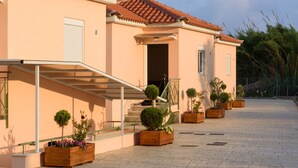 Un edificio con tejado de tejas, un porche cubierto y una escalera que conduce a una puerta. Hay jardineras de madera con arbustos y flores a lo largo del camino.