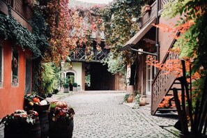 A cobblestone courtyard with a wooden staircase on the right, surrounded by buildings with ivy-covered walls. - Pêche de Vigne & Spa (Rodern)