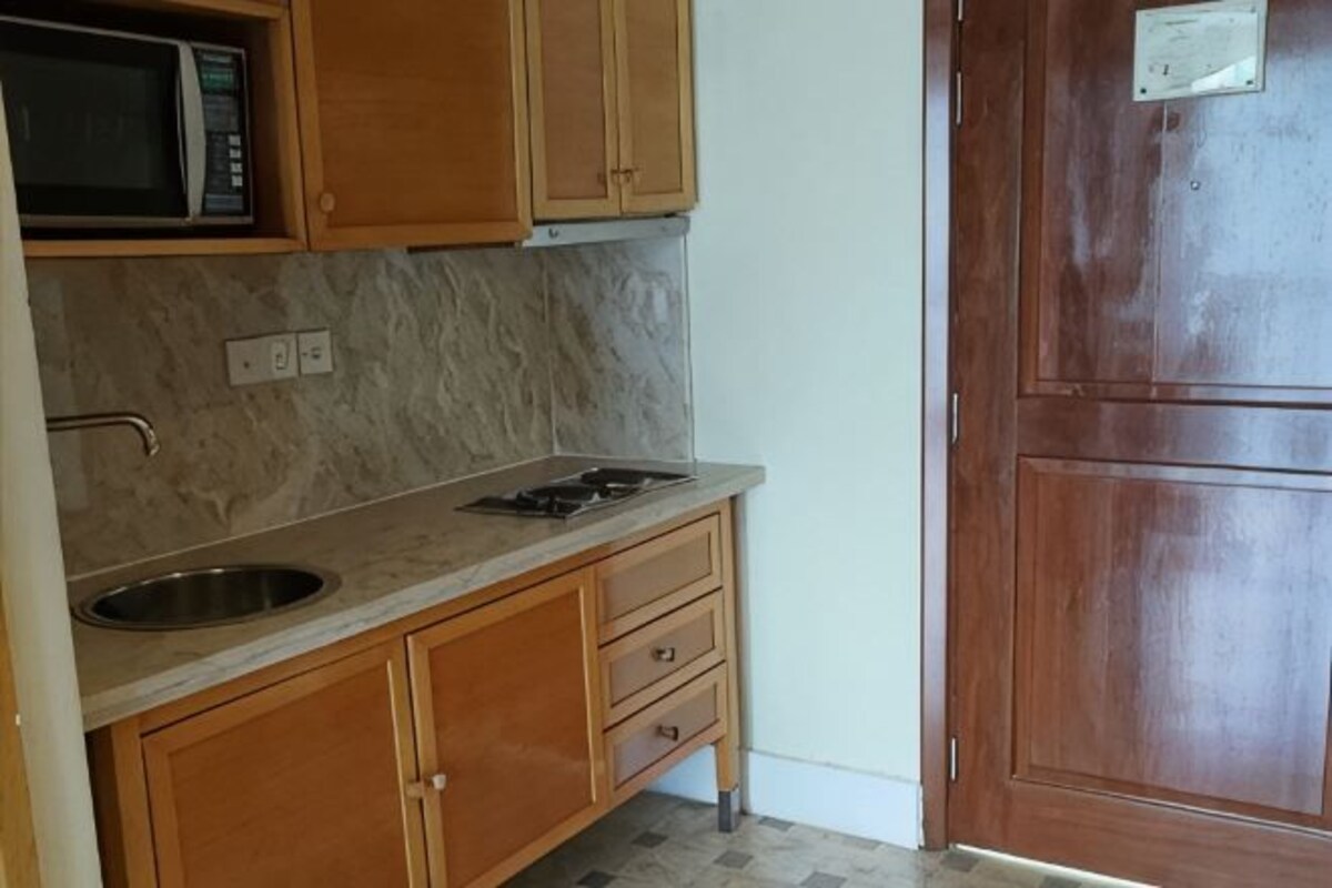 Una cocina con armarios de madera, encimera de mármol, pileta de acero inoxidable y microondas.