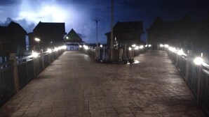 Une vue nocturne d’une promenade dallée, bordée de lampadaires régulièrement espacés, et flanquée de bâtiments à l’architecture traditionnelle.