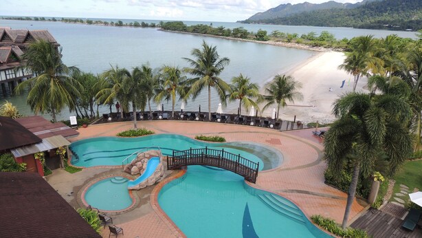 Un complexe hôtelier doté d’une grande piscine, de palmiers et offrant une vue sur la plage.