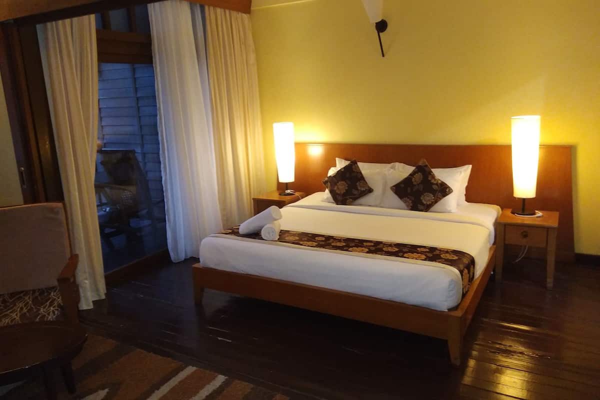 Een hotelkamer met een groot bed, twee bedlampen, een houten hoofdbord en uitzicht door een schuifdeur.