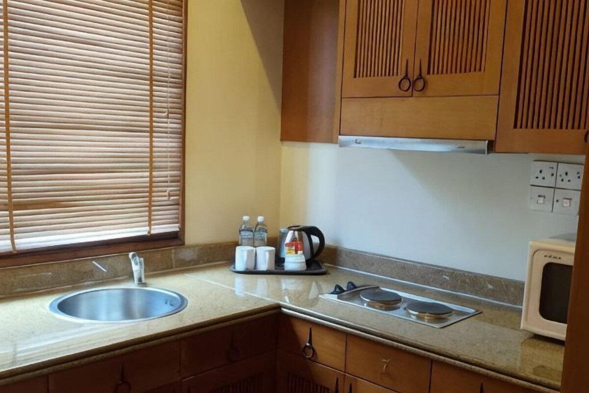 A kitchen with wooden cabinets, a stainless steel sink, a microwave, and a window with blinds.