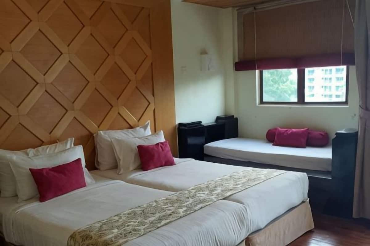 Een hotelkamer met twee bedden, een houten hoofdbord, een raam met uitzicht en een bankje bij het raam.