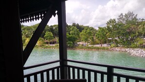 Une terrasse en bois avec un banc donnant sur une étendue d’eau, le tout entouré d’une végétation luxuriante et d’arbres.