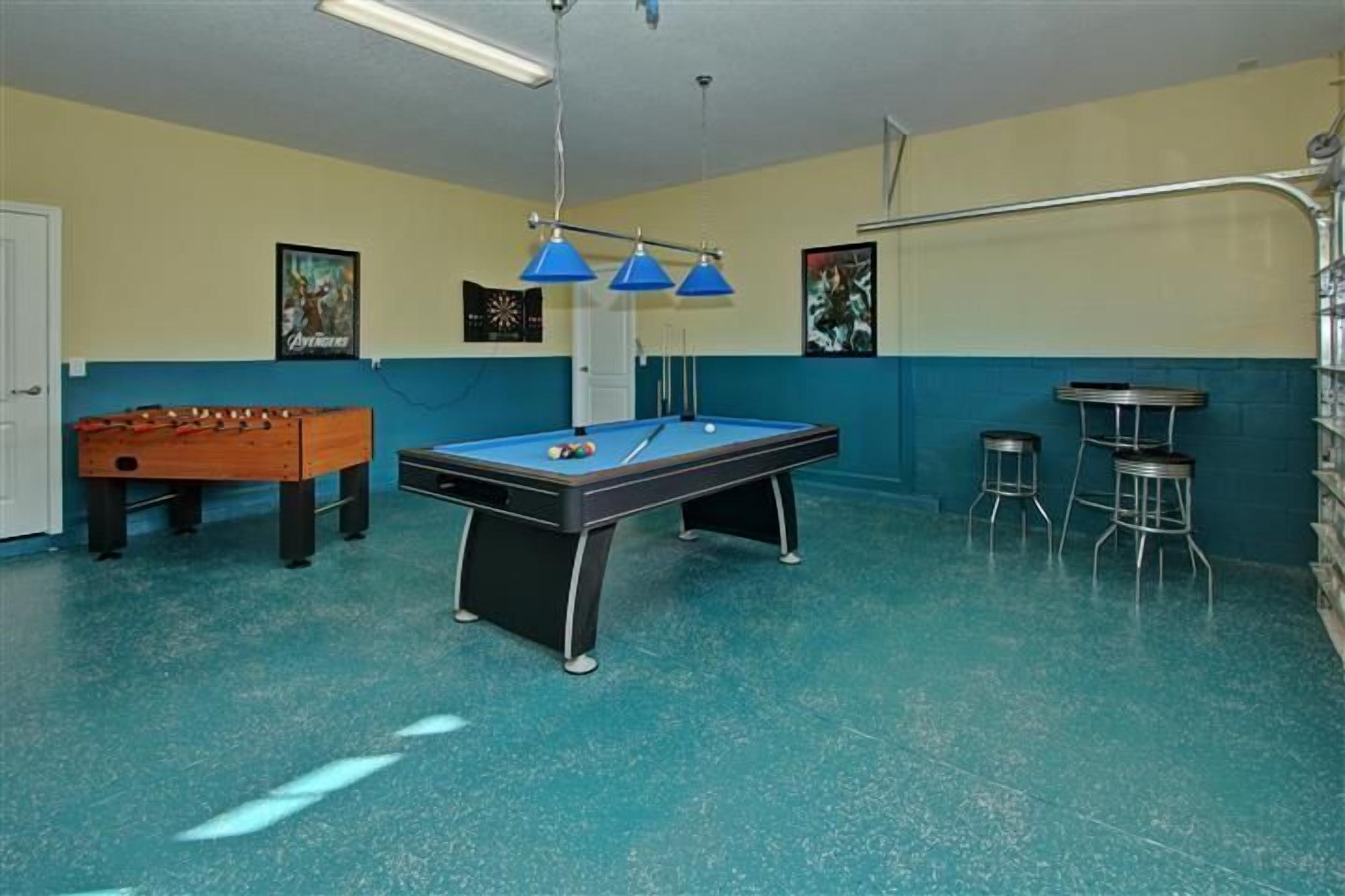 A room with a pool table, foosball table, and two bar stools.