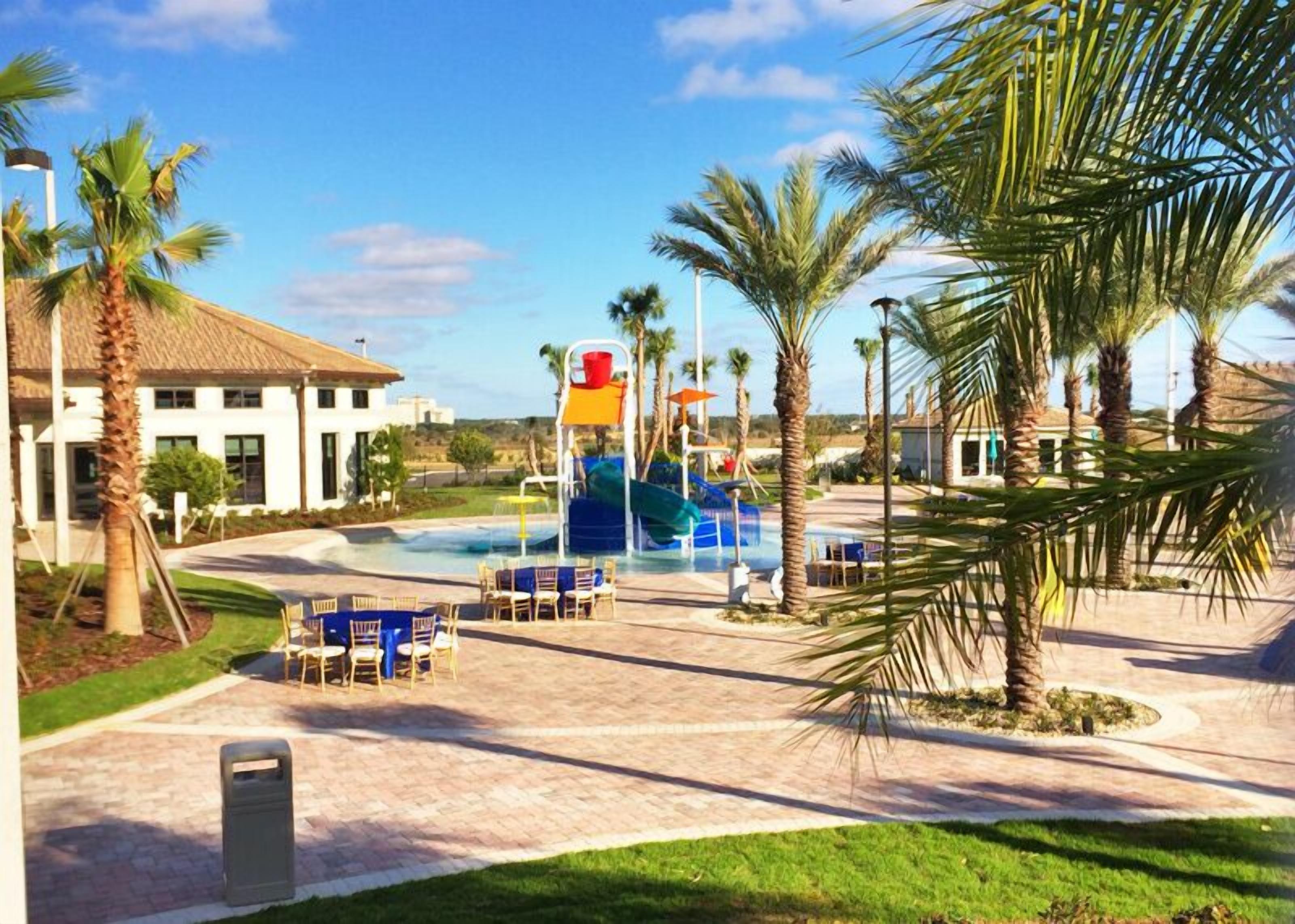 A resort pool area with palm trees, a water slide, and lounge chairs.