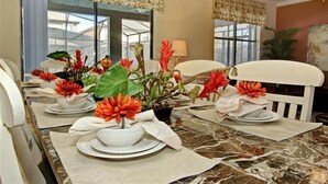 Ein Esstisch ist gedeckt mit weißen Tellern, Servietten und einer Blumenarragemet aus orangen Blüten.
