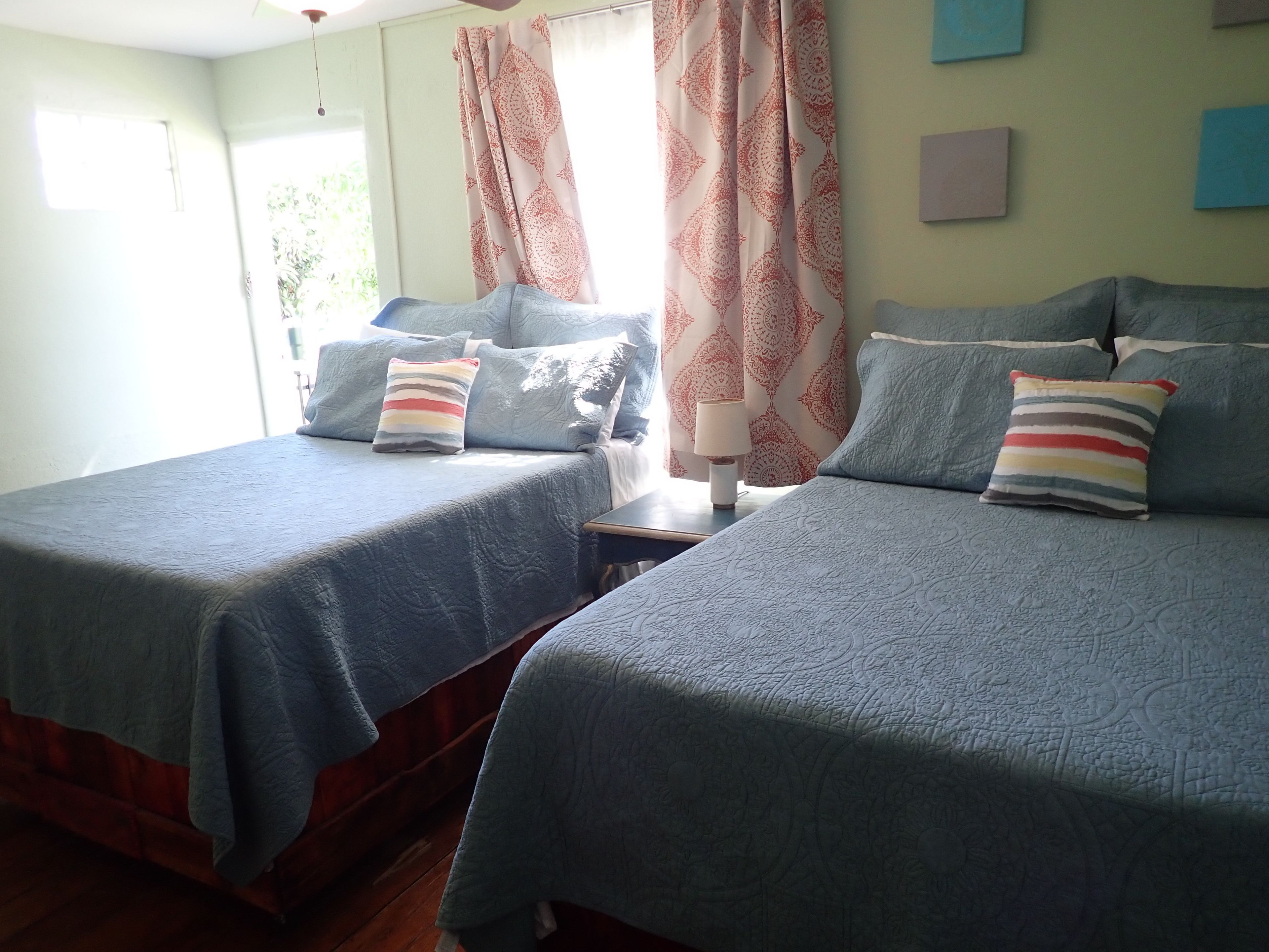 Une chambre avec deux lits, chacun recouvert d’une courtepointe bleue et agrémenté d’oreillers à rayures. Une table de chevet avec une lampe se trouve entre les deux lits.