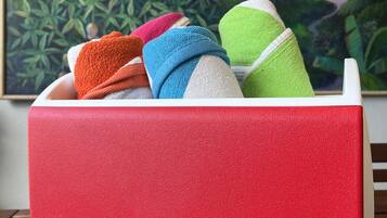 A red IGLOO cooler with colorful towels inside, placed on a wooden table with a painting of a tropical scene in the background.