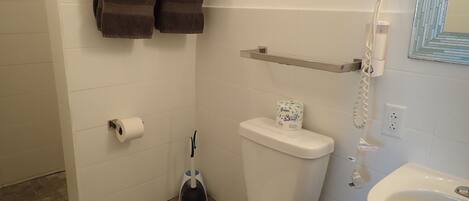 A bathroom with a toilet, a sink, a towel rack with towels, a toilet paper holder, a hairdryer, and a trash bin.