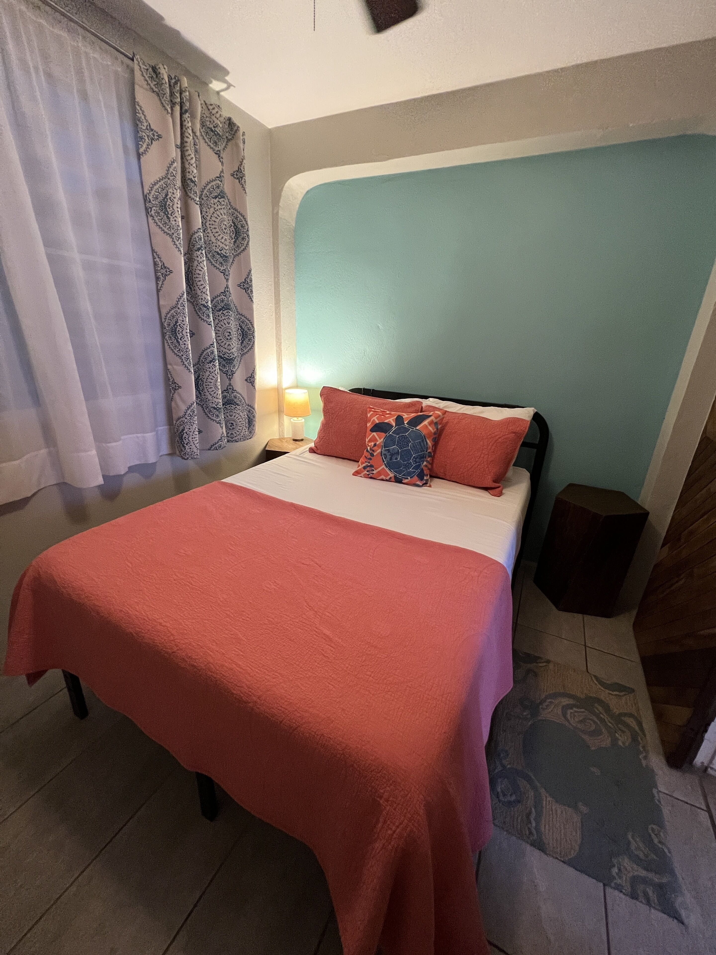A bed with a red blanket, a pillow with a turtle design, and a nightstand with a lamp.