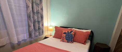 A bed with a red blanket, a pillow with a turtle design, and a nightstand with a lamp.