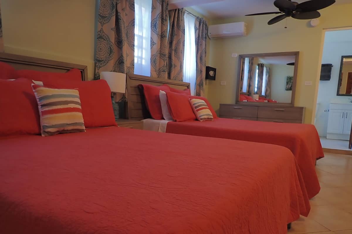 A hotel room with two beds, a ceiling fan, an air conditioning unit, a mirror, and a dresser.