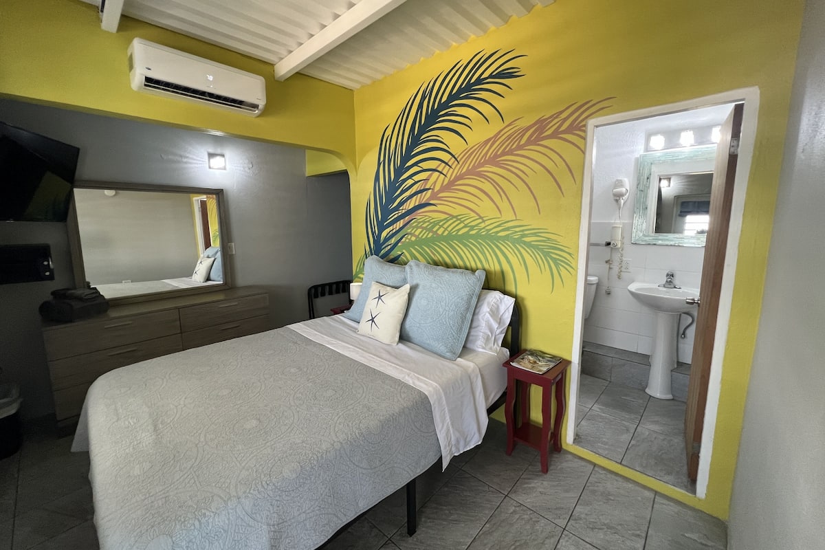 A hotel room with a bed, a nightstand, a mirror, a sink, and an air conditioning unit.