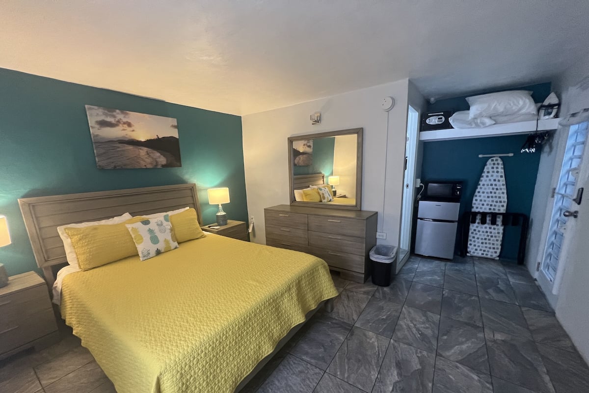 A hotel room with a bed, bedside tables, a mirror, a small kitchenette, and a bathroom.