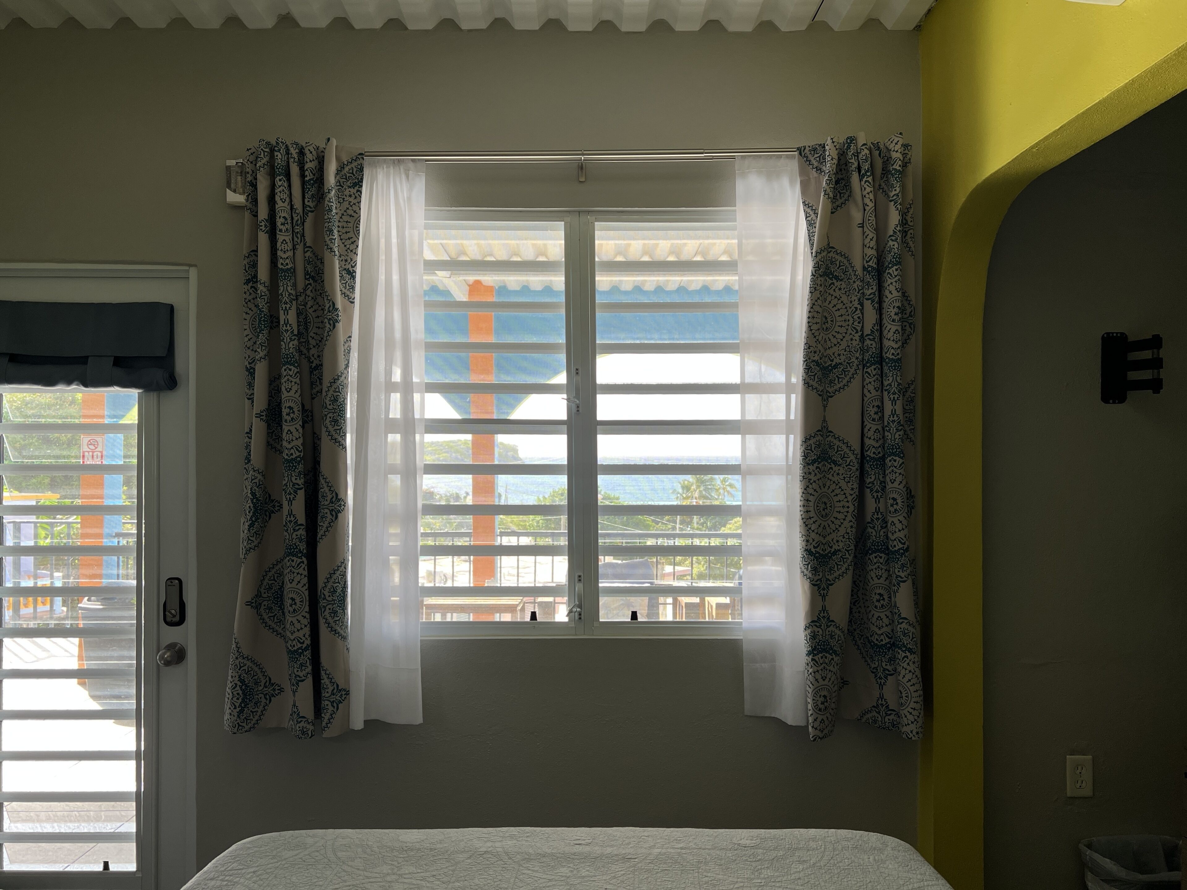 Une chambre avec un lit, une fenêtre ornée de rideaux à motifs et une vue sur l’extérieur.