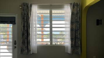 A room with a bed, a window with patterned curtains, and a view of the outside.