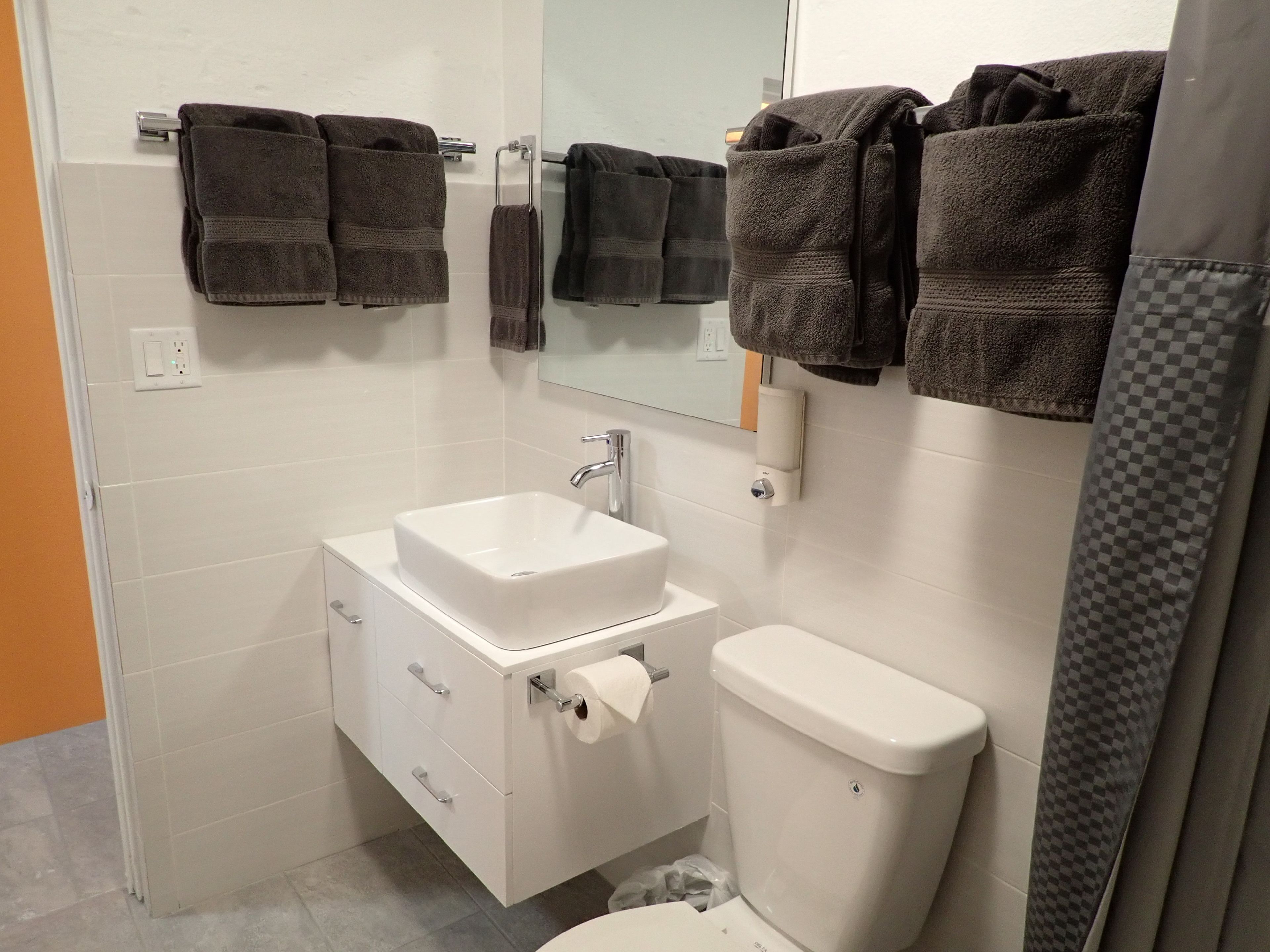 Ein Badezimmer mit einem weißen Waschbecken, einem Spiegel, einer Toilette und mehreren Handtüchern an einem Ablagekorb.
