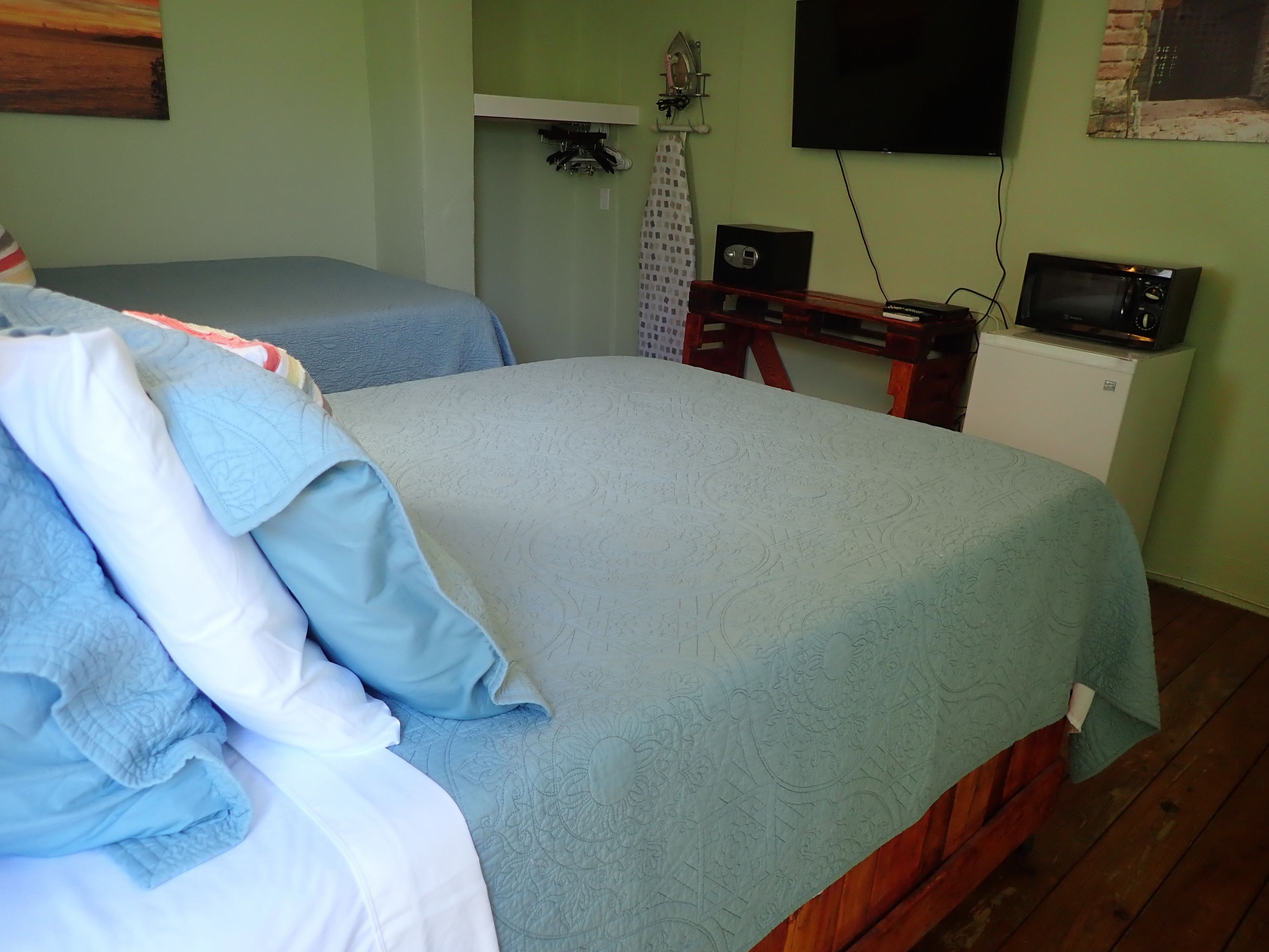 A bedroom with two beds, a small white cabinet, a television, and a wall-mounted ironing board.