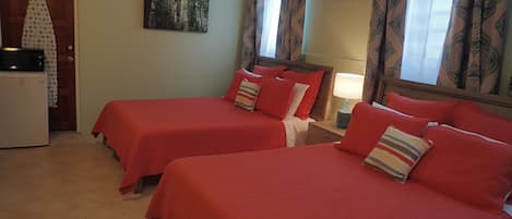 A hotel room with two beds, a ceiling fan, a microwave, and a painting on the wall.
