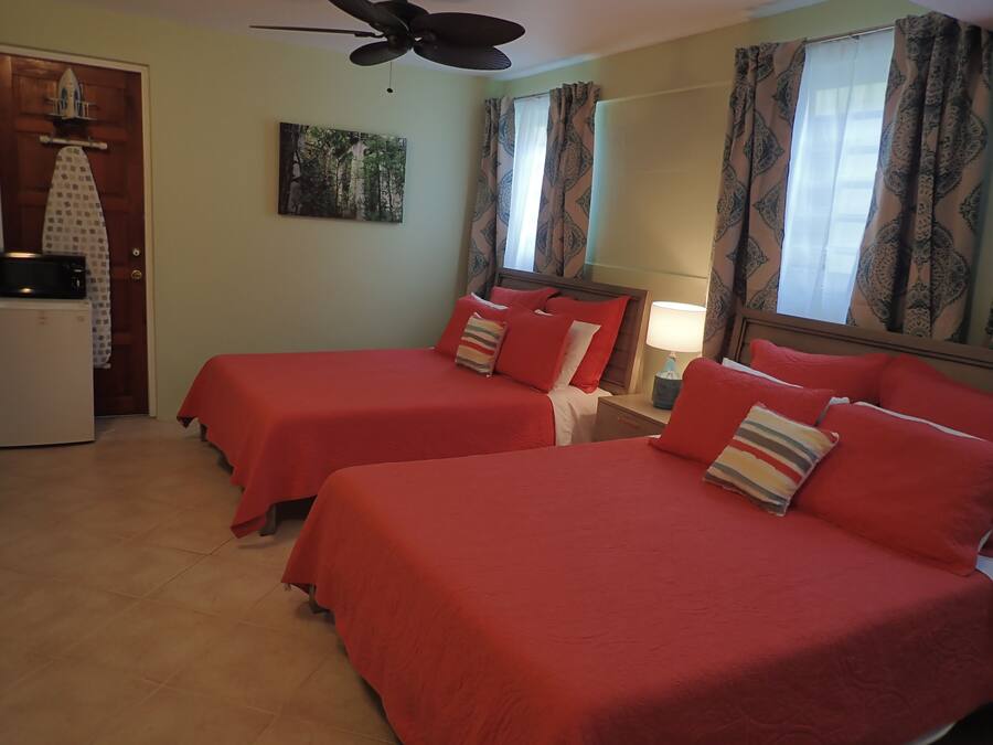 A hotel room with two beds, a ceiling fan, a microwave, and a painting on the wall.