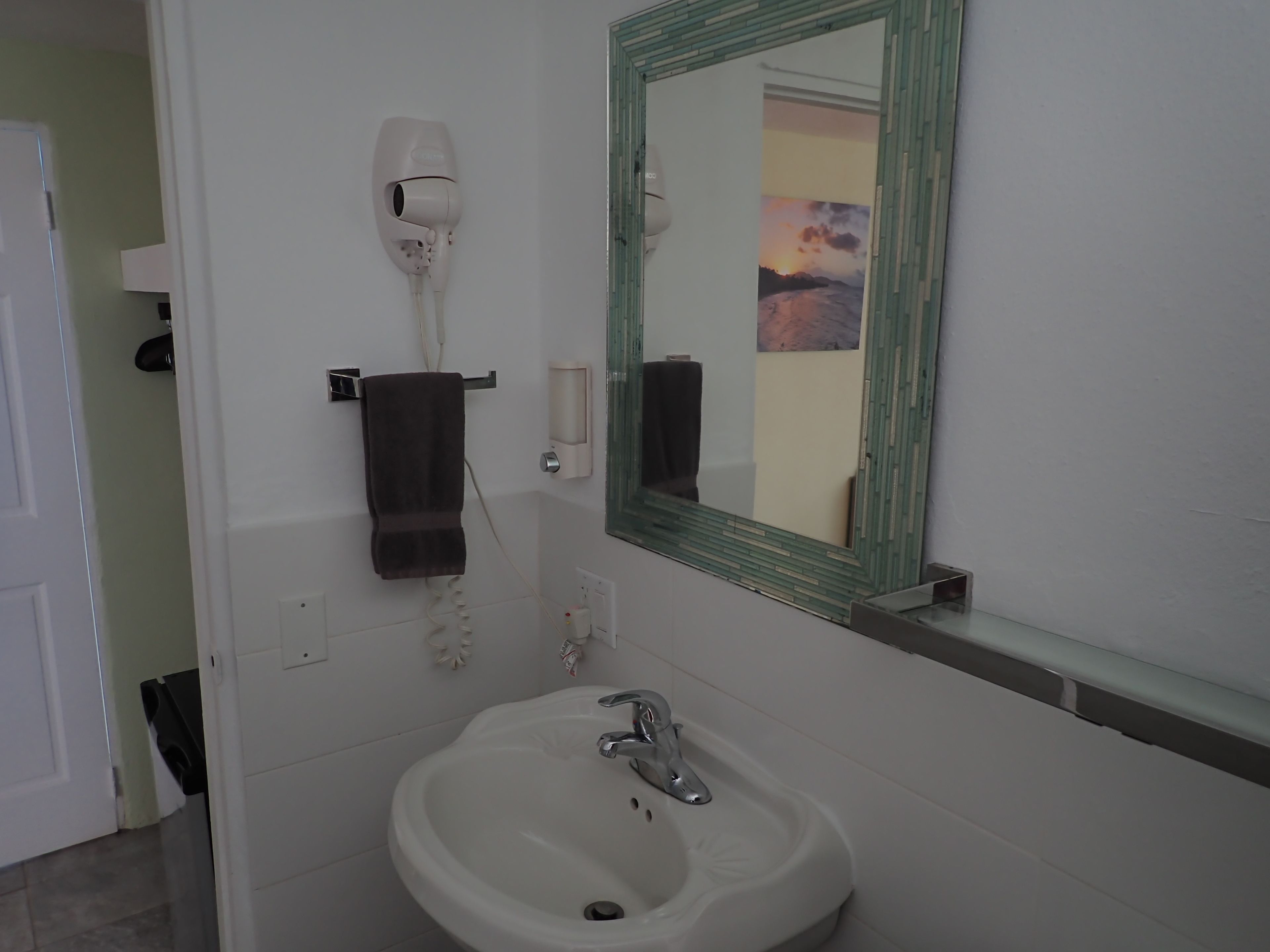 Ein Badezimmer mit einem weißen Waschbecken, einem Spiegel mit grünem Rahmen und einem an der Wand montierten Föhn.