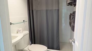 A bathroom with a toilet, a glass shelf, a shower curtain, and towels hanging on a rack.