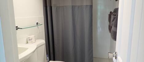Un baño con inodoro, repisa de vidrio, cortina de ducha y toallas colgadas en un perchero.