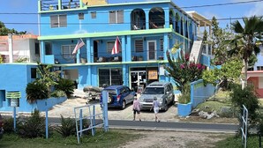 A two-story building with a blue facade, a balcony, and a flag. - The Vieques Guesthouse (Vieques)