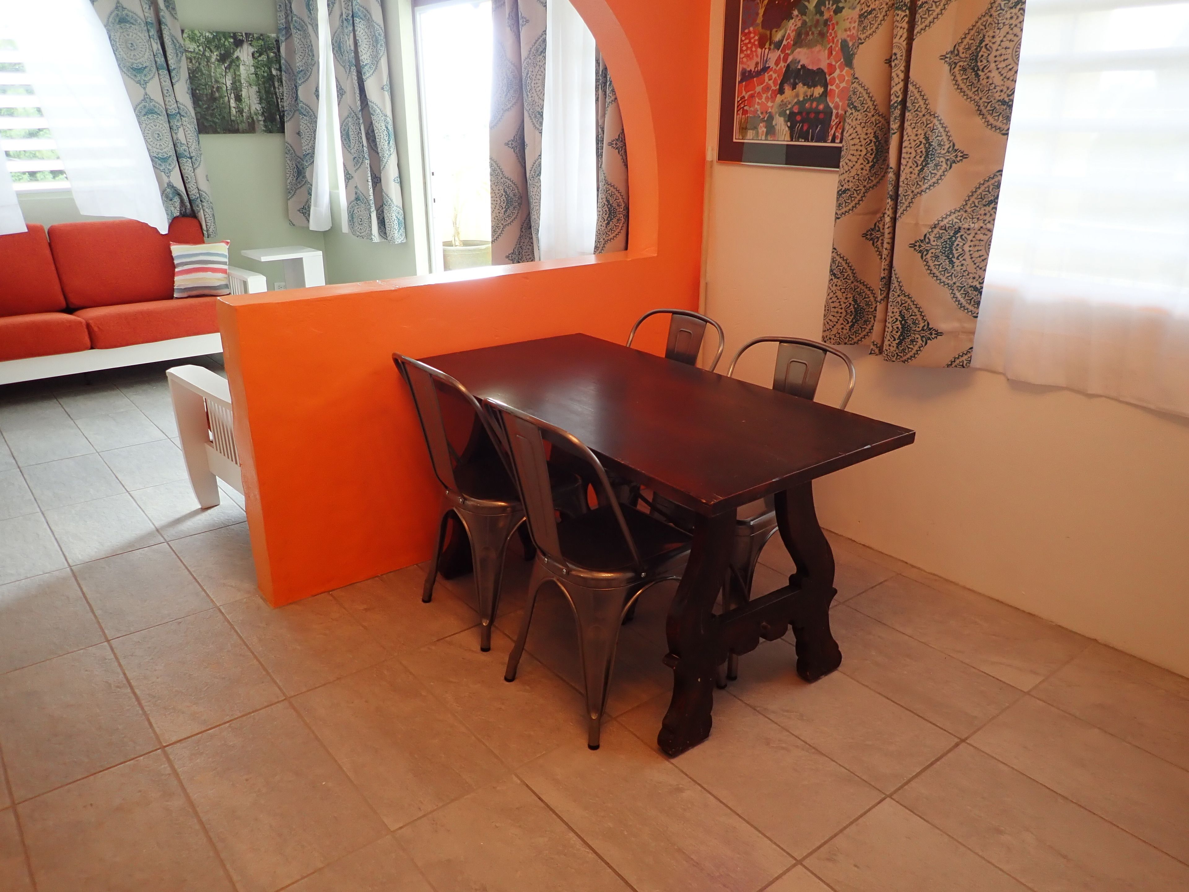 Un comedor con una mesa y sillas de madera, un sofá rojo y cortinas estampadas.