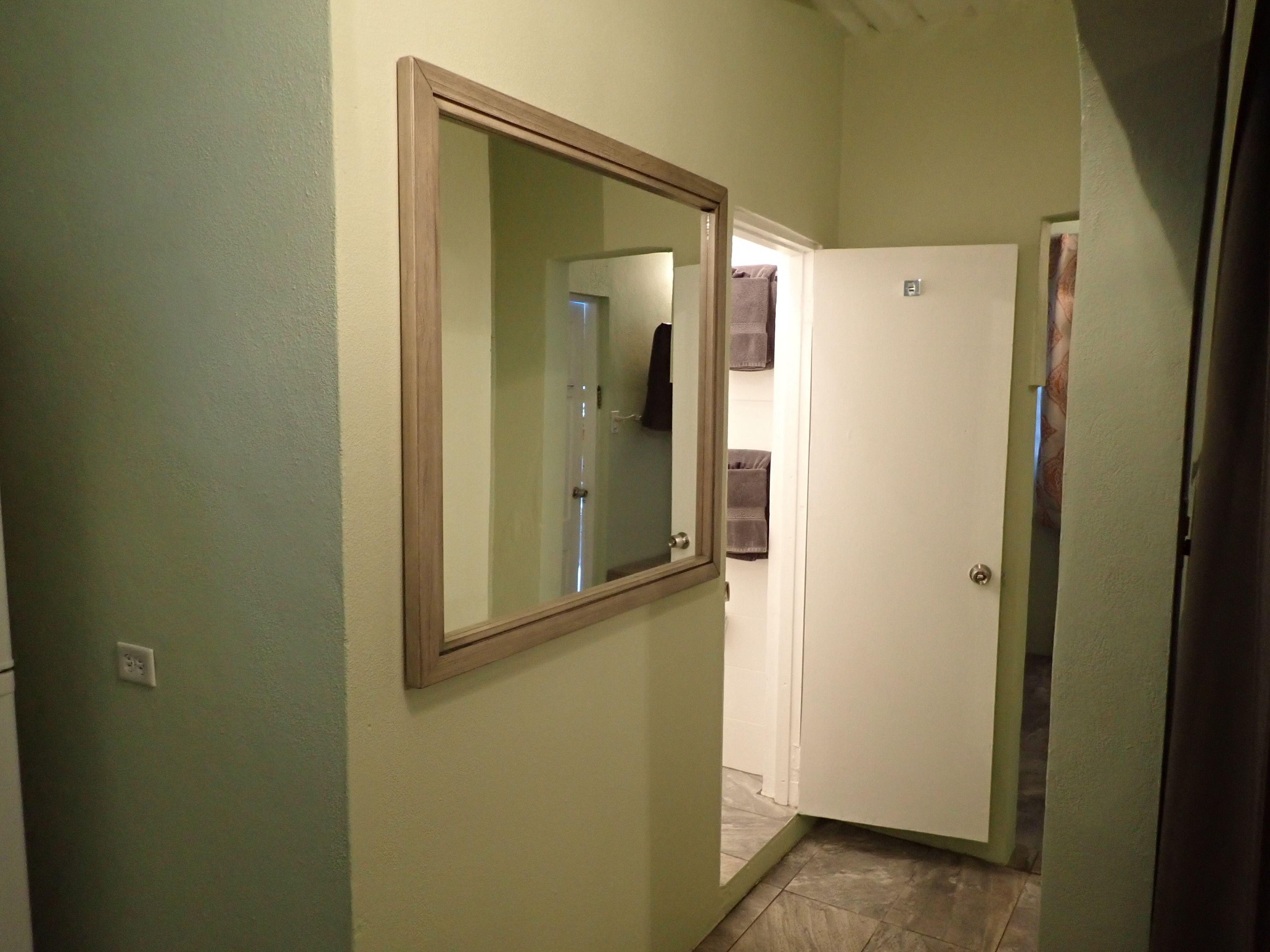 Un pasillo estrecho con una puerta blanca y un espejo en la pared.