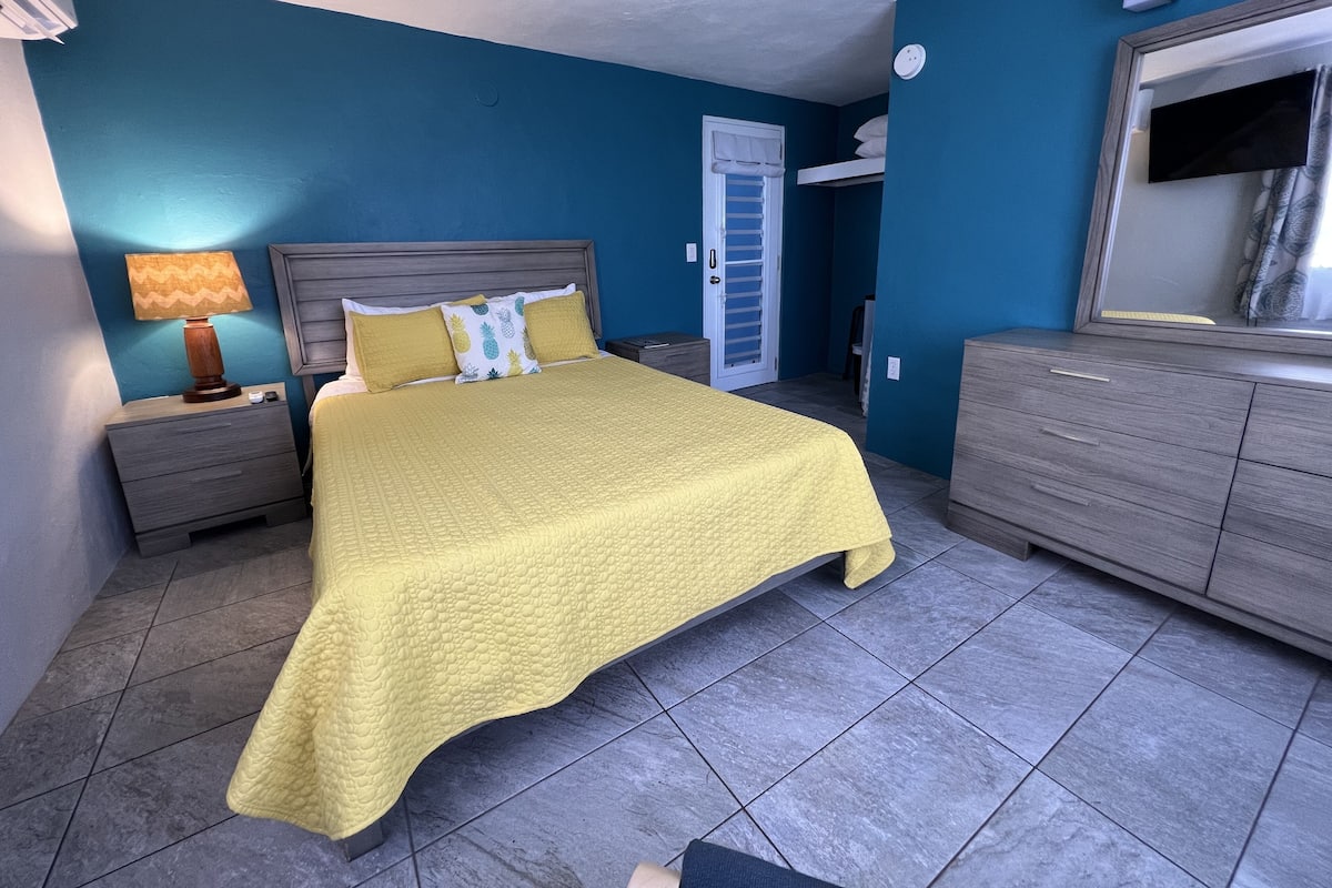 A bedroom with a bed, nightstands, a dresser, a mirror, and a door.