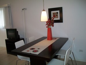 Un coin repas comprenant une table, des chaises, un vase avec des fleurs, un téléviseur et un tableau encadré accroché au mur.