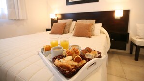 Una habitación de hotel con una cama bien hecha, una bandeja con alimentos para el desayuno y dos lámparas de noche.