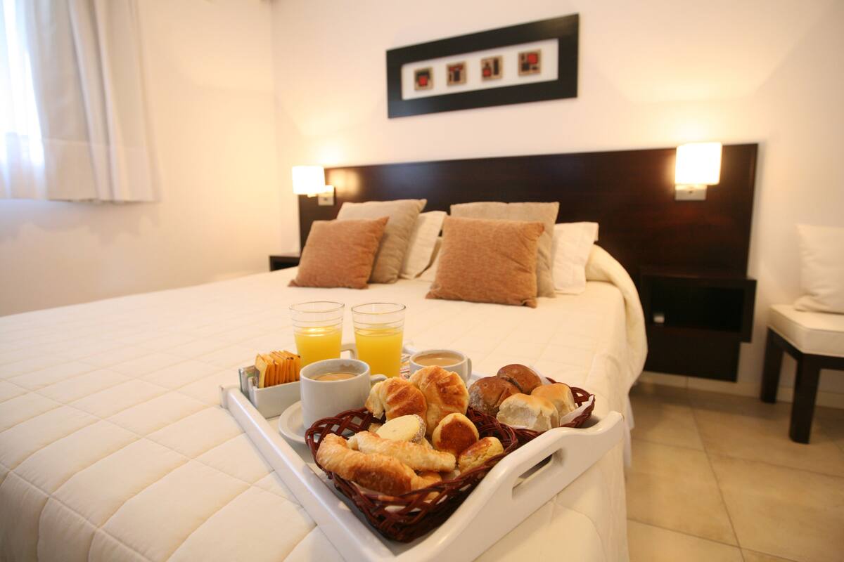 Una habitación de hotel con una cama bien hecha, una bandeja con alimentos para el desayuno y dos lámparas de noche.