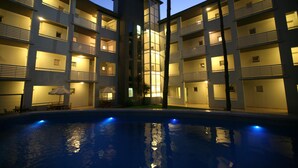 Un hotel de varios pisos con balcones, piscina y mobiliario de exterior.