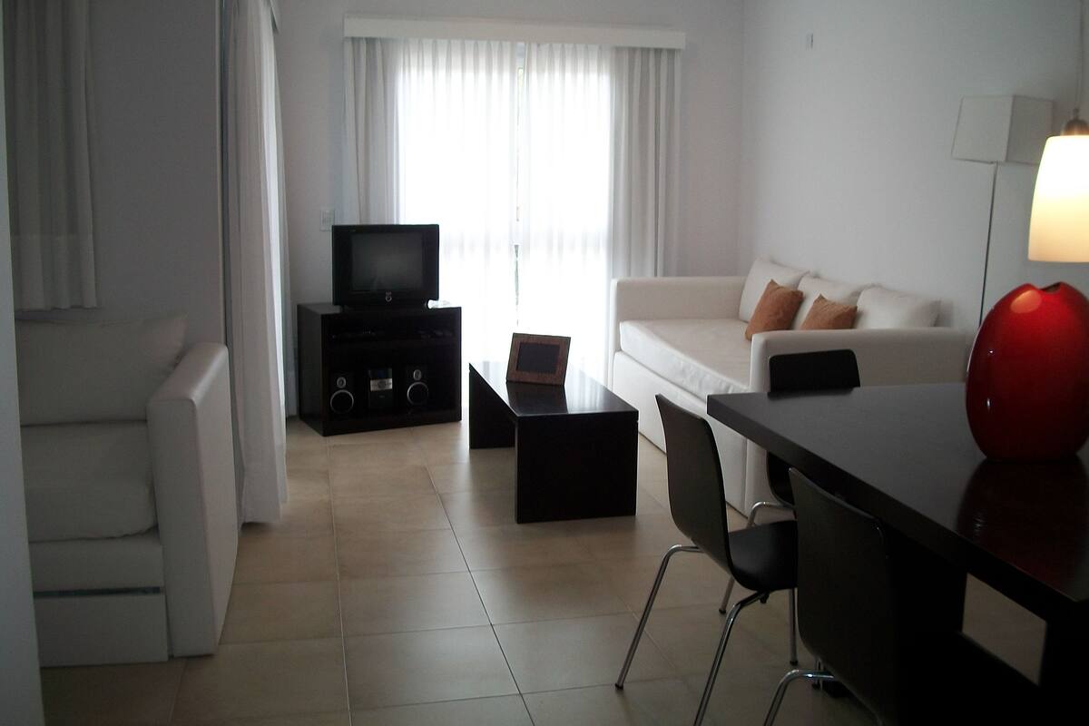 Una sala de estar moderna con una televisión de pantalla plana, un sofá, una mesa de centro y un escritorio con una lámpara.