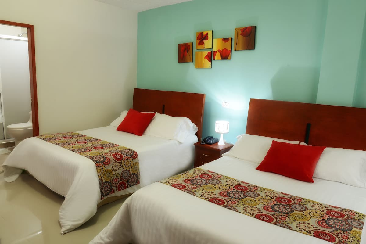 Dos camas con ropa de cama roja y blanca, una mesita de noche con lámpara, y una pared decorada con motivos florales.