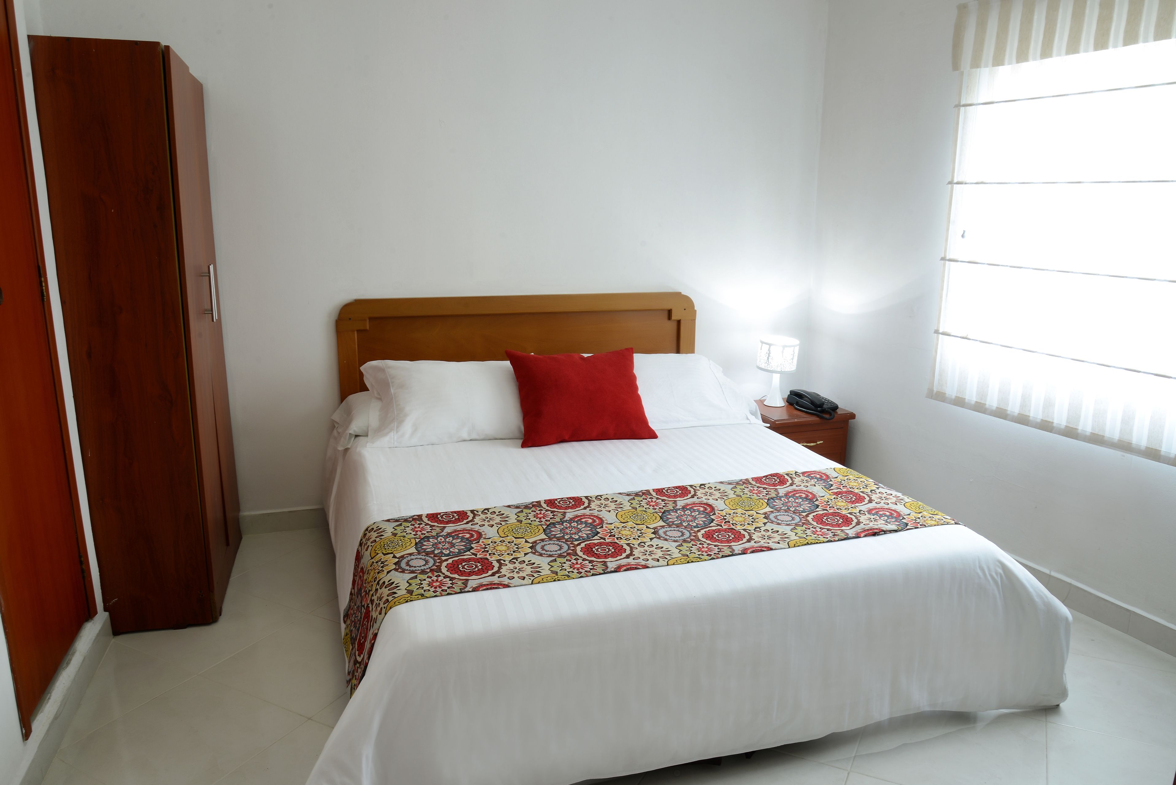 Una cama bien hecha con una colcha estampada, un cabecero de madera y una almohada roja.