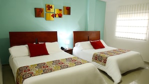Habitación de hotel con dos camas, cada una con un almohadón rojo y una colcha estampada. Se observan obras de arte en las paredes sobre las camas y una ventana con persianas a la derecha.