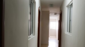 Un pasillo estrecho y bien iluminado con suelo de baldosas y paredes blancas, que conduce a una habitación con ventana.