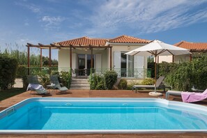 Ein Schwimmbad mit Liegestühlen und Sonnenschirmen, eine überdachte Terrasse und ein Haus mit einem Ziegeldach.