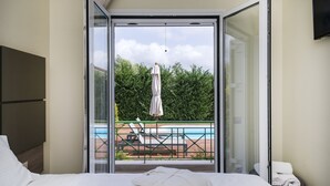 A hotel room with a bed, a view of a pool and lounge chairs, and a sliding glass door. - Jewel of Venus Villa - Private Pool Paradise (Pylos-Nestoras)