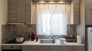A modern kitchen with a built-in stove, a sink, and a window with sheer curtains. - Jewel of Venus Villa - Private Pool Paradise (Pylos-Nestoras)